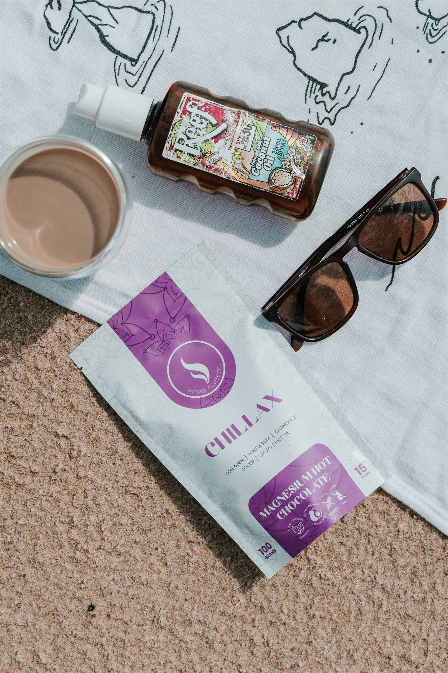 Chillax hot chocolate on a beach towel with sunscreen and sunglasses